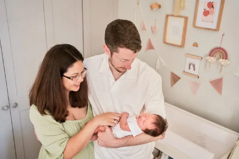 Parents admiring their newborn beside the cot in a softly decorated nursery