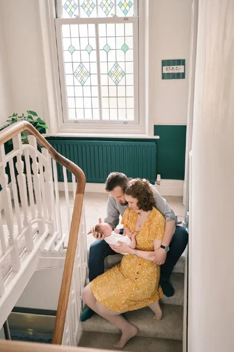 Parents cradling their baby together on the sunlit stairs at home